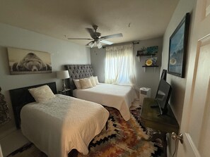 Camera da letto con due letti, una ventola a soffitto, un comodino con una lampada, un tappeto e opere d'arte alle pareti.