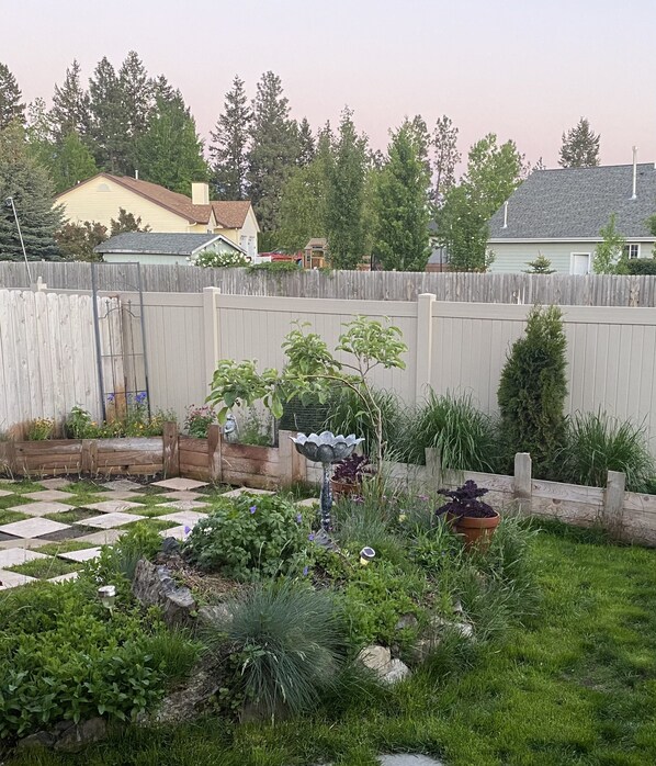 A backyard with a wooden fence, a garden with various plants and flowers, and a paved walkway.
