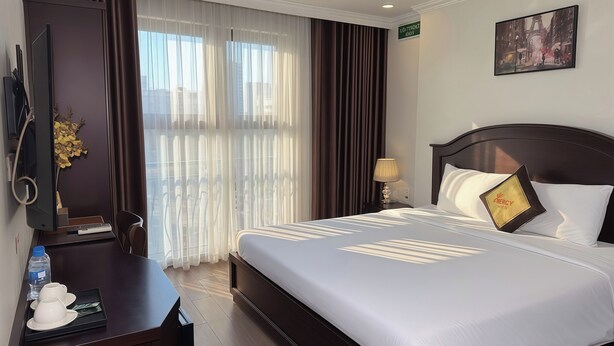 Una habitación de hotel con cama, escritorio con computadora, lámpara y un cuadro en la pared.
