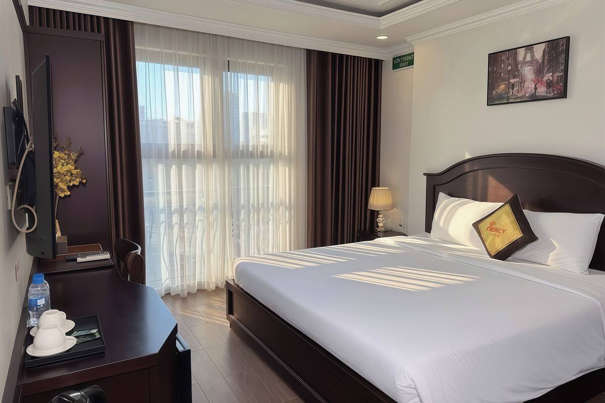 Una habitació d'hotel amb un llit, una taula de treball amb un ordinador, una làmpada i un quadre a la paret.