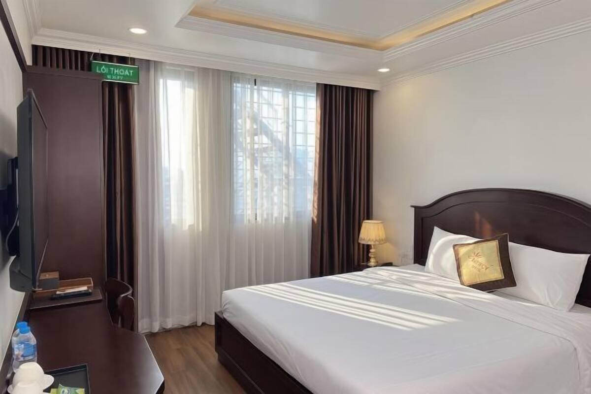 Habitació d'hotel amb llit, escriptori, televisió i cortines.