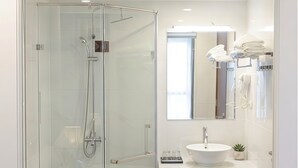 Un baño moderno con ducha envuelta en vidrio, un lavamanos blanco y un espejo sobre él.