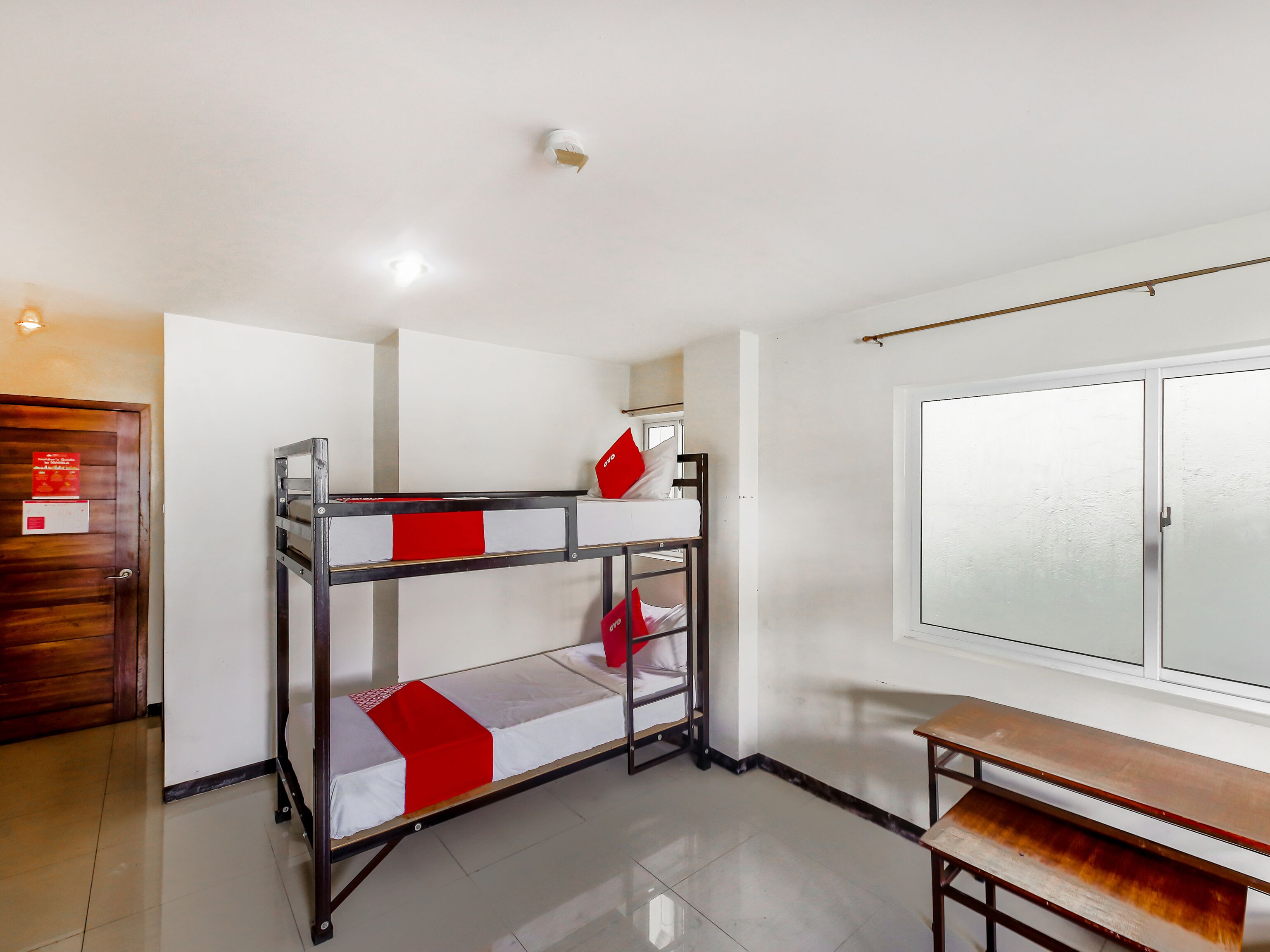 A bunk bed with a red and white bedspread, a wooden bench, and a wardrobe with frosted glass doors.