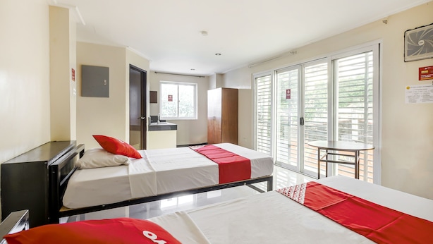 A hotel room with two beds, a desk, a small kitchenette, and a balcony with a table. - Vaccinated Staff - OYO 850 Clr Mn Inn (Quezon City)