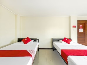 A hotel room with two single beds, each with a red and white bedspread and matching pillows. The room has cream-colored walls and a wooden door. - Vaccinated Staff - OYO 850 Clr Mn Inn (Quezon City)