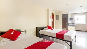 A hotel room with two beds, each with white bedding and red accents, a small bedside table, a wall-mounted TV, and a window providing natural light. - Vaccinated Staff - OYO 850 Clr Mn Inn (Quezon City)
