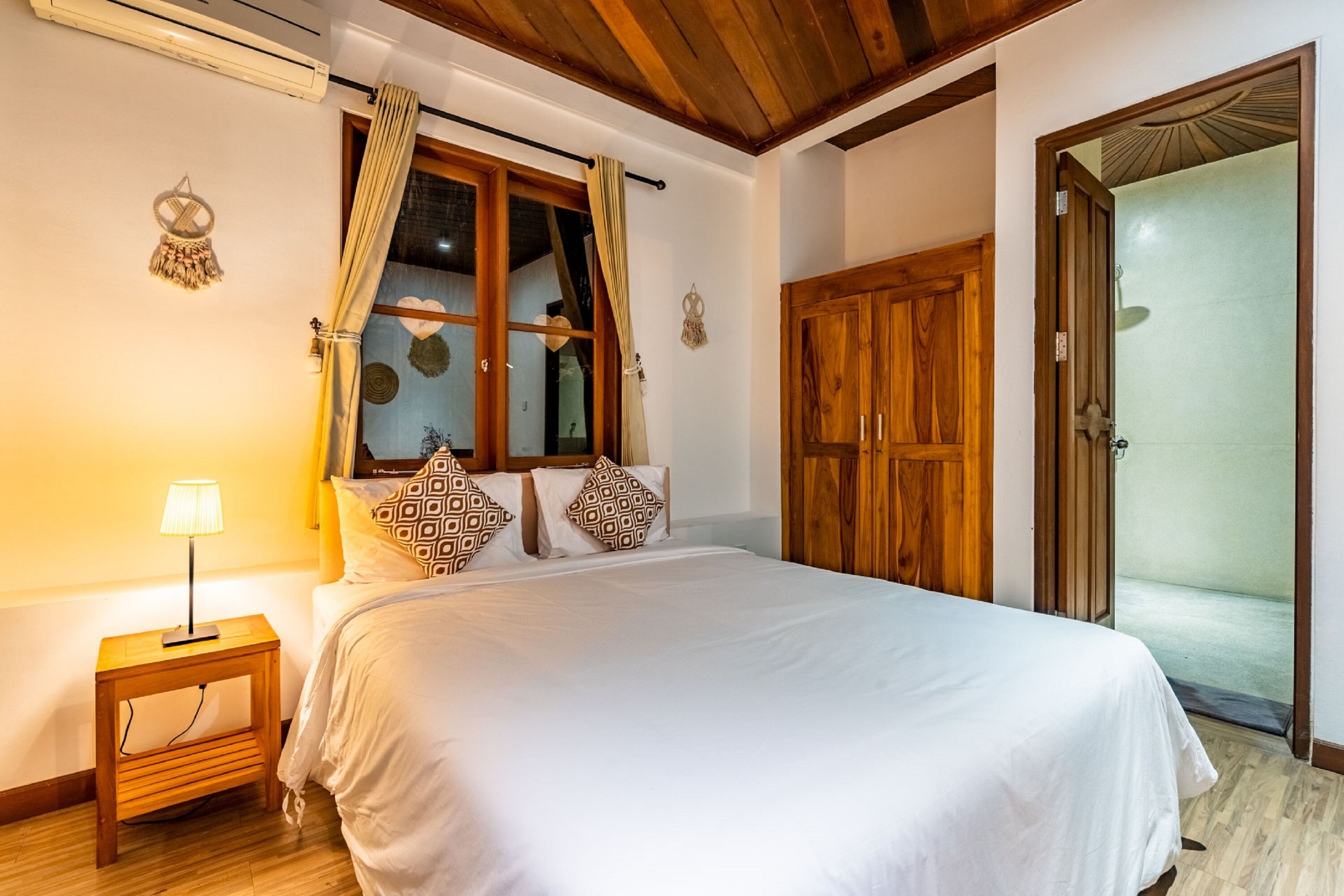 A bedroom with a bed, wooden wardrobe, and a window with curtains.