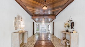 A hallway with a stone floor, wooden ceiling beams, and two console tables with decorative items. - AV Villa Canggu Hearts (Canggu)
