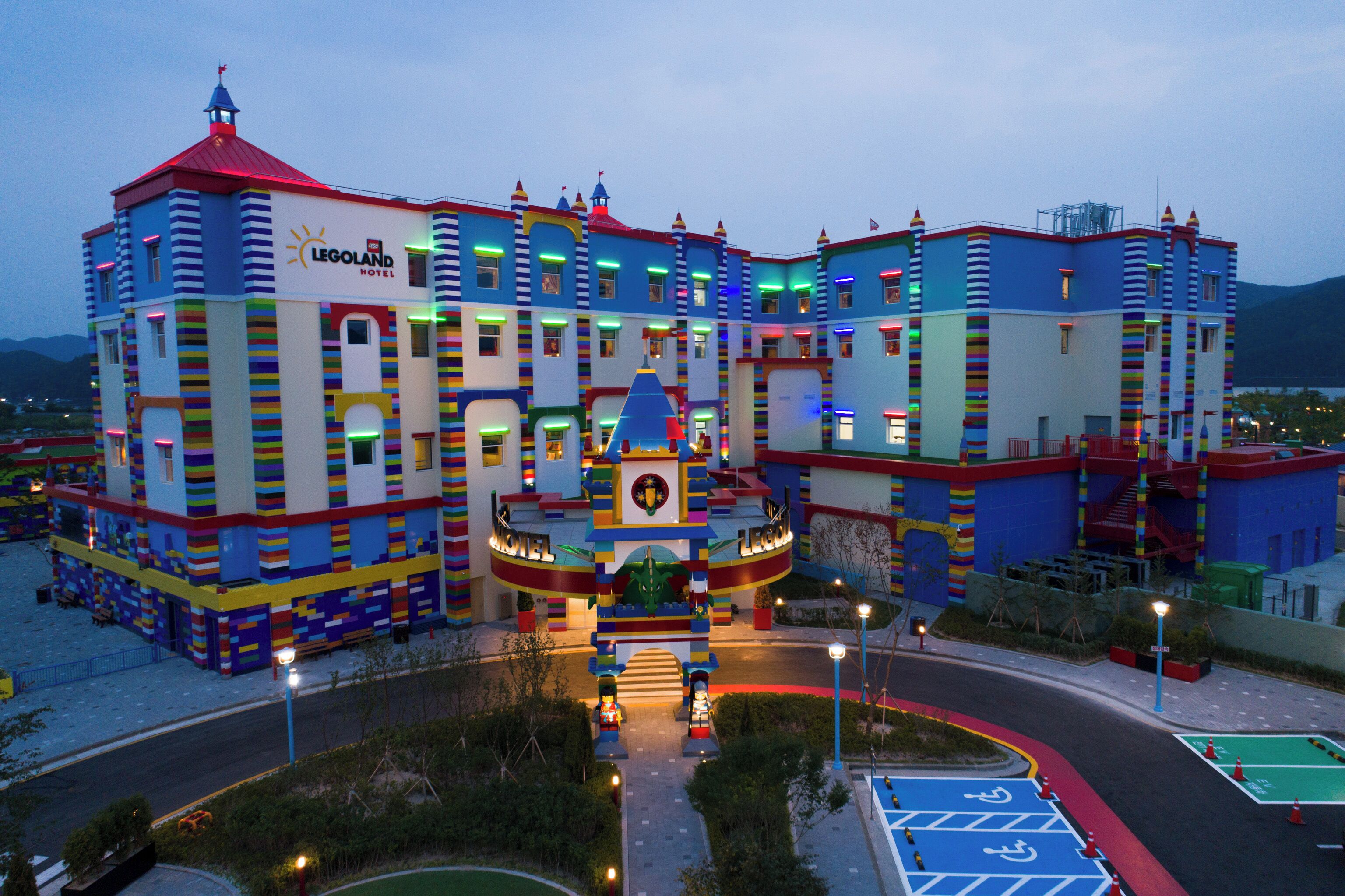 Un hotel colorido con una torre central y varias alas, que presenta una entrada destacada y un estacionamiento con espacios para discapacitados.
