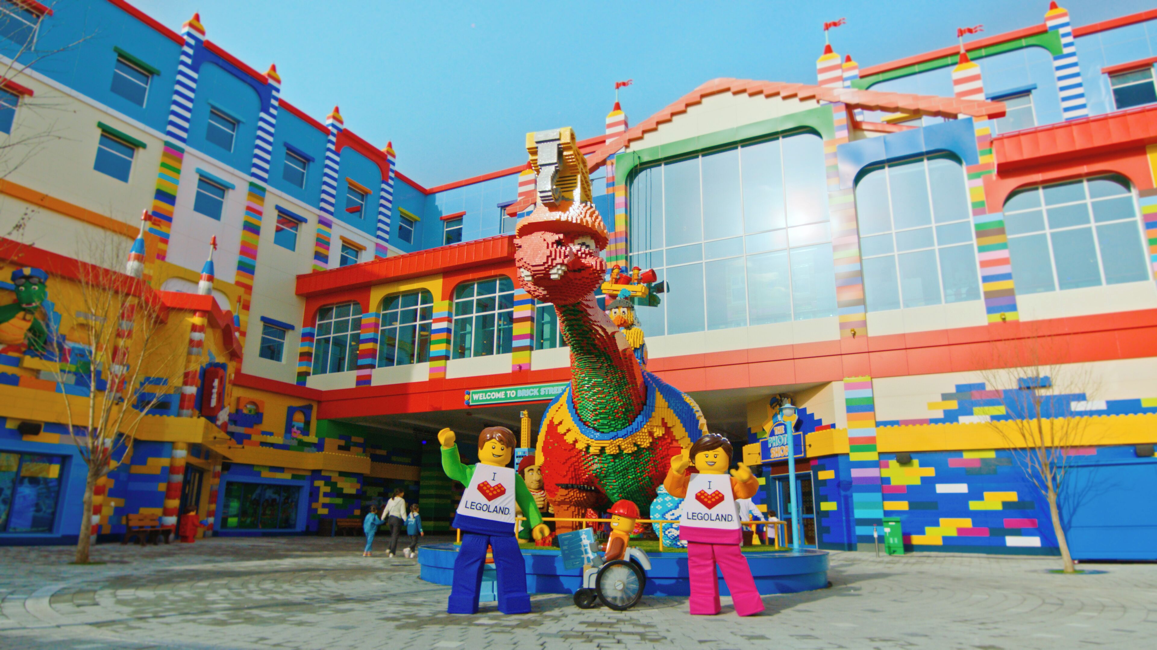 A colorful LEGO display with a dragon and figures in front of a building with a sign reading "Welcome to Brick Street."