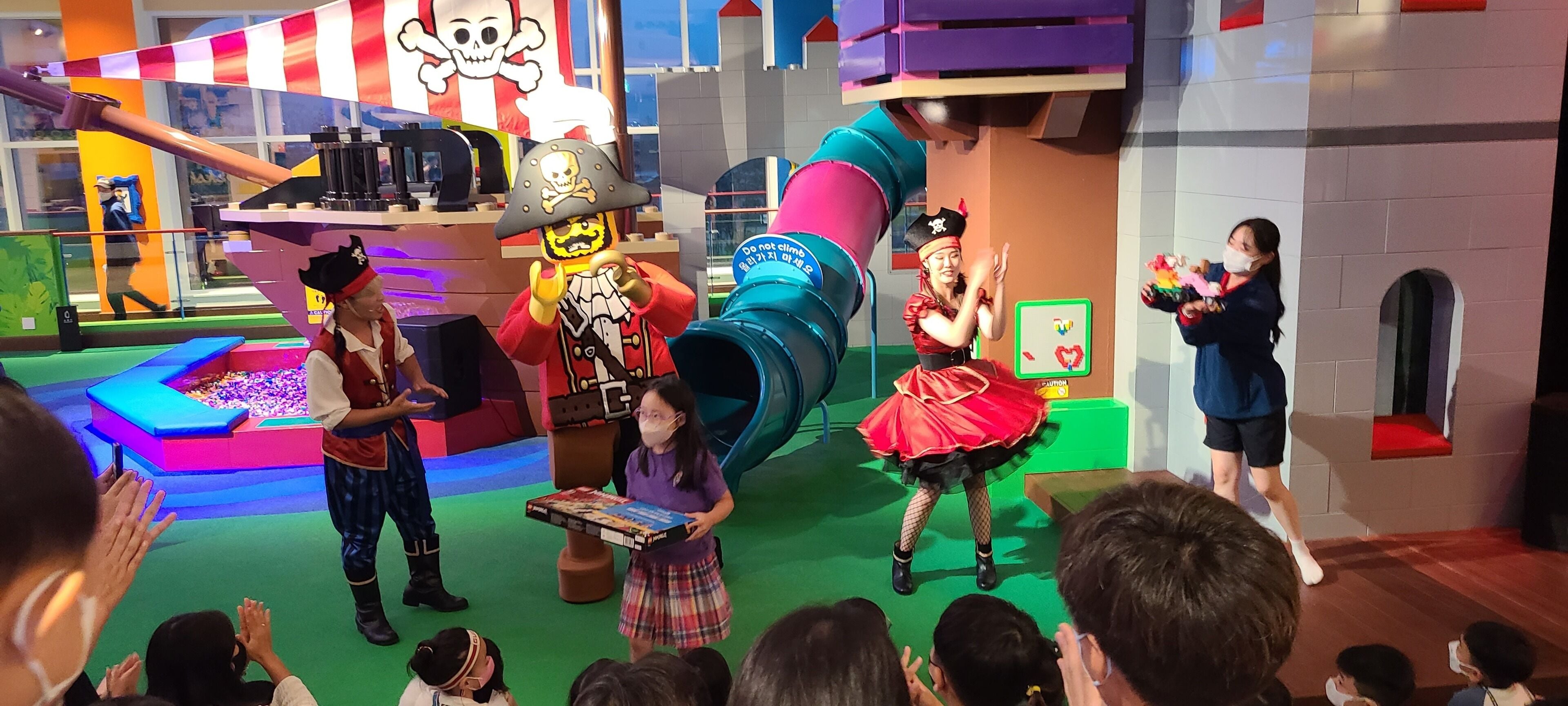 A colorful indoor play area with a slide, a pirate-themed character, and children engaged in activities.