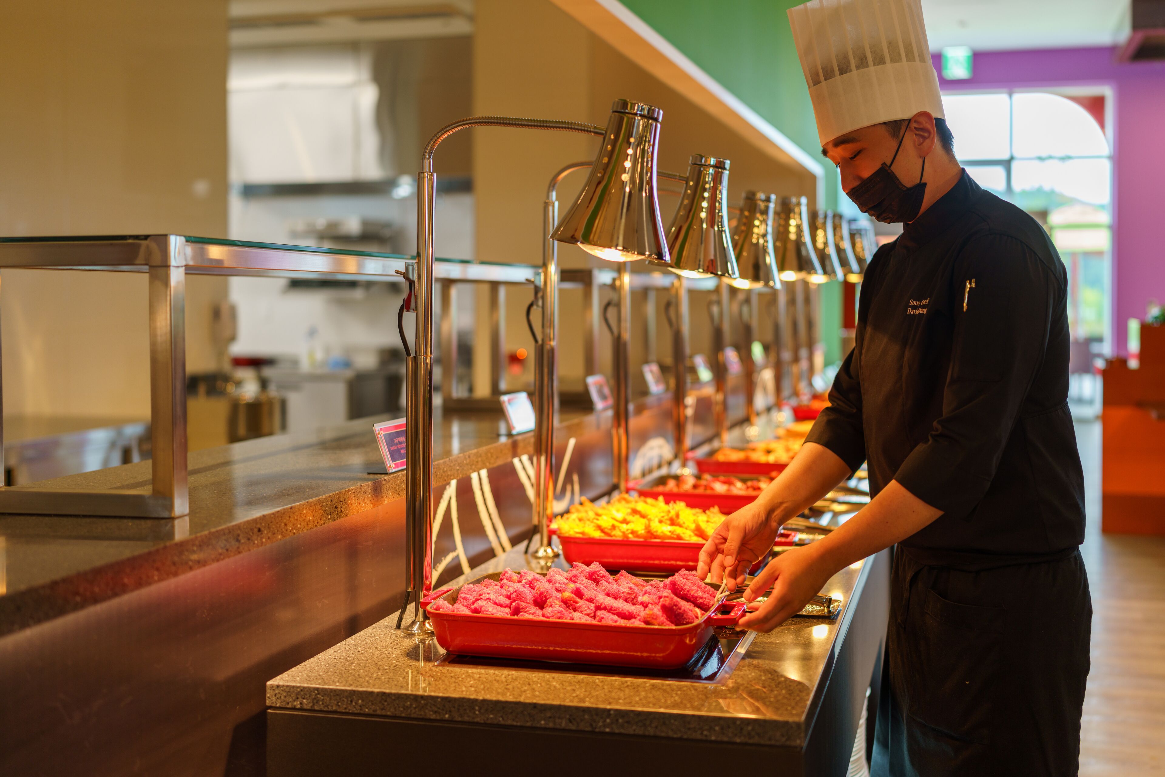 A buffet setup with various food items and a person serving.