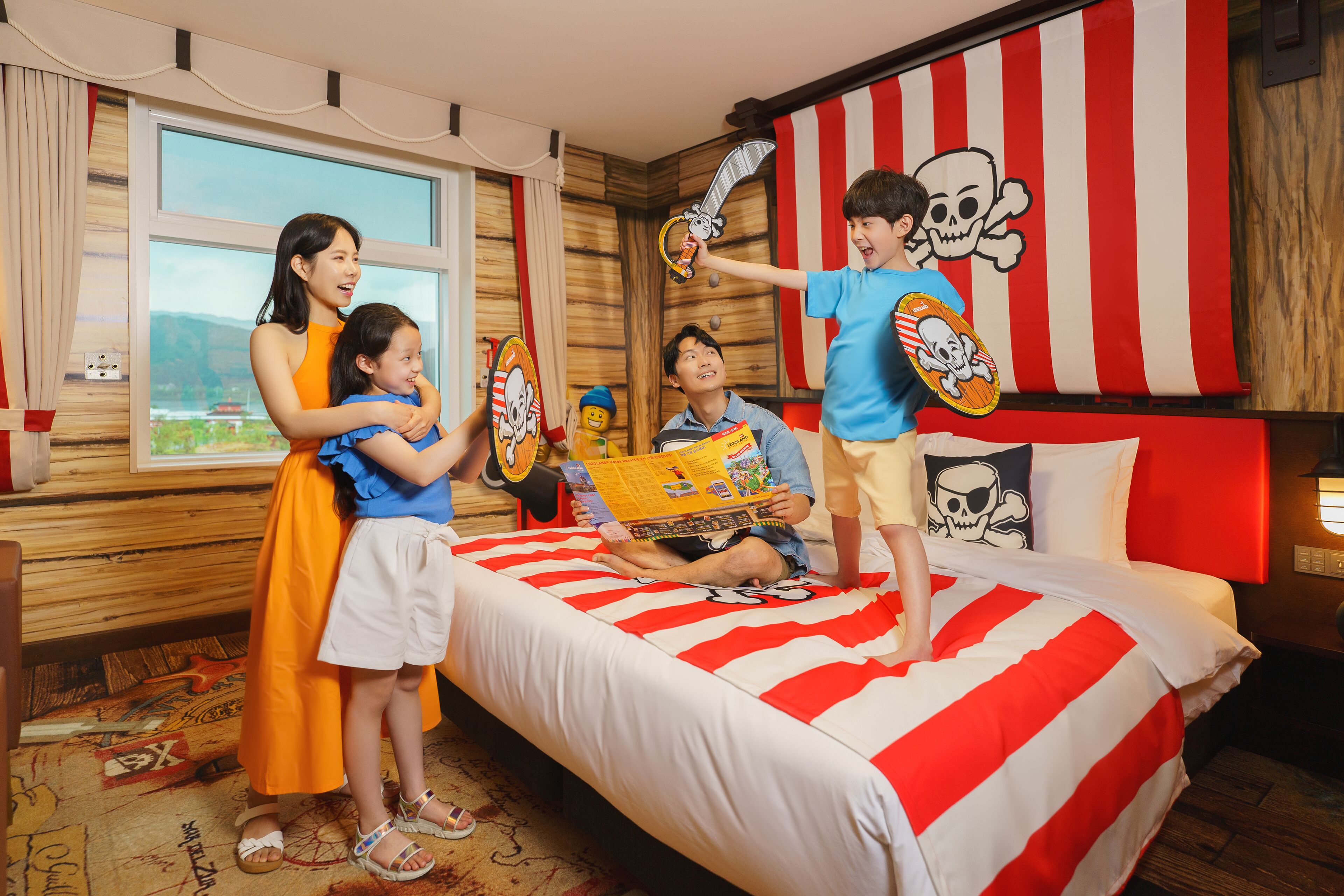 A room with a bed featuring a red and white striped bedspread, a wooden wall, and a large window.