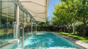 A swimming pool with clear blue water, surrounded by glass walls and a covered patio area.
