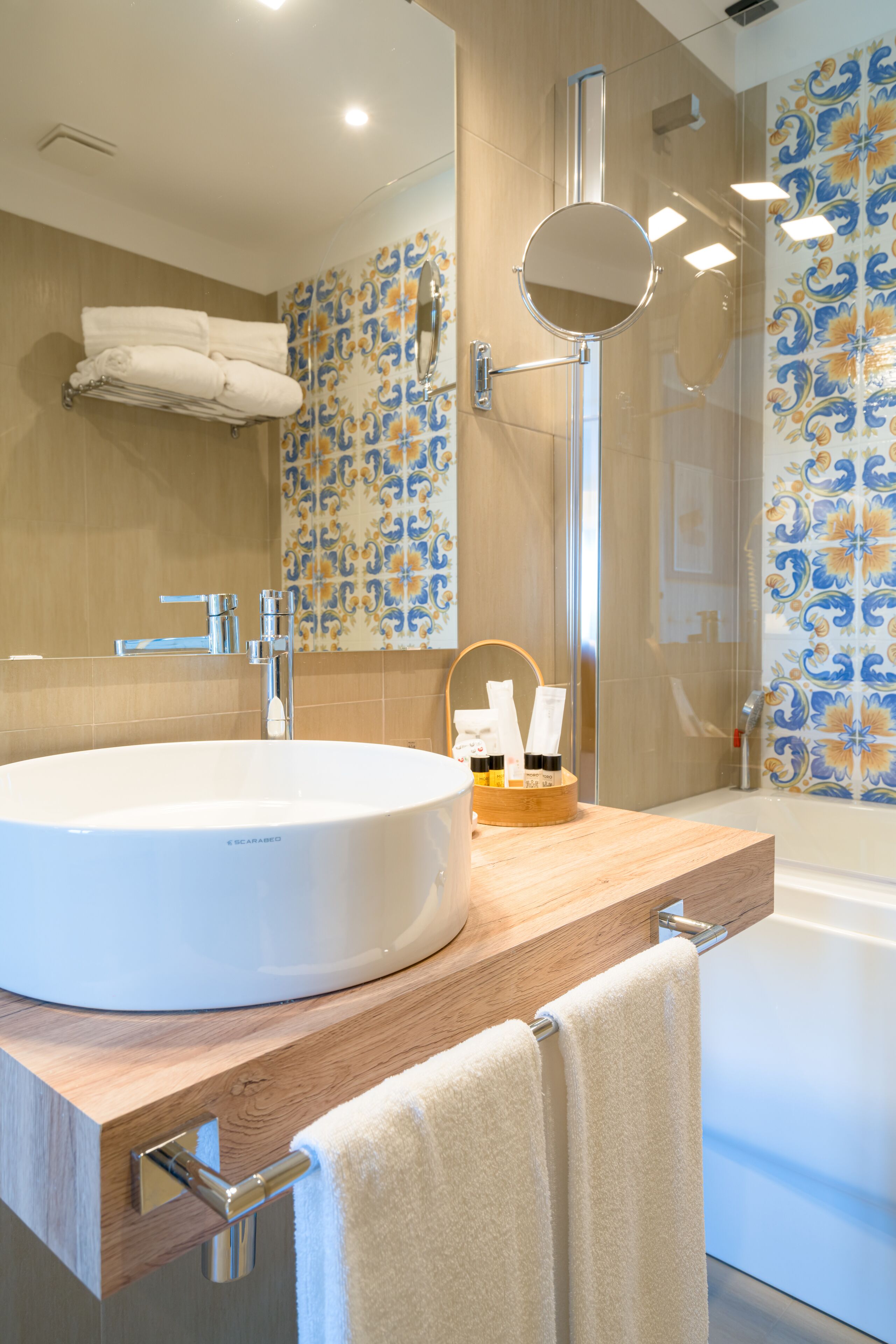 A modern bathroom with a large white sink, a wooden vanity, a glass shower enclosure, and patterned tiles.