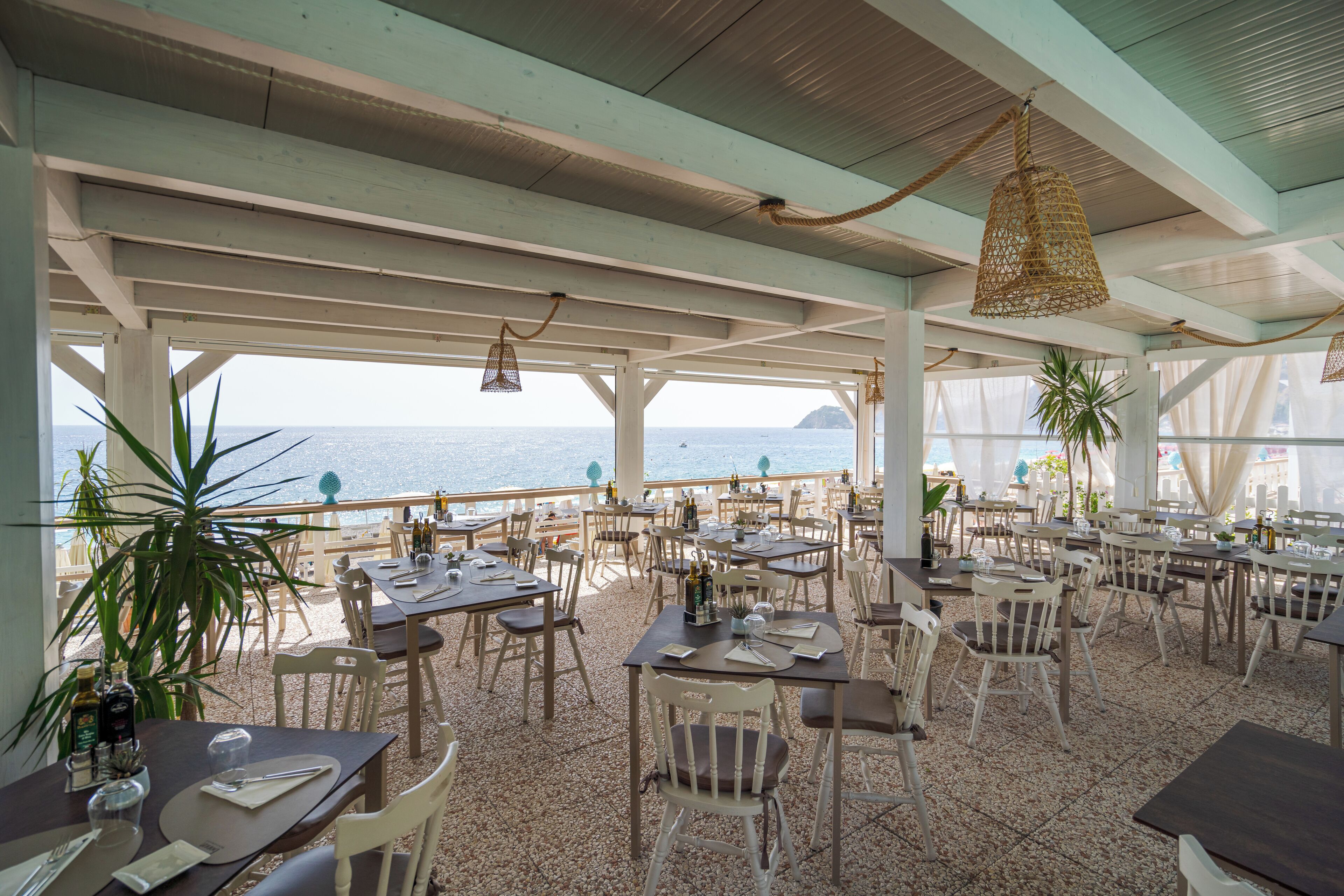 An outdoor dining area with tables and chairs, overlooking the sea.