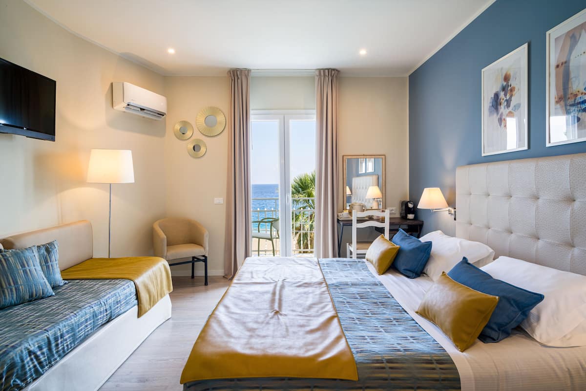 Habitación de hotel con cama, sofá, escritorio y vistas al mar.