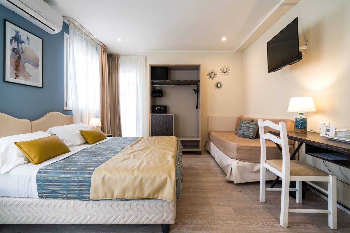 Habitación de hotel con una cama, un escritorio, una silla, un televisor y un armario.