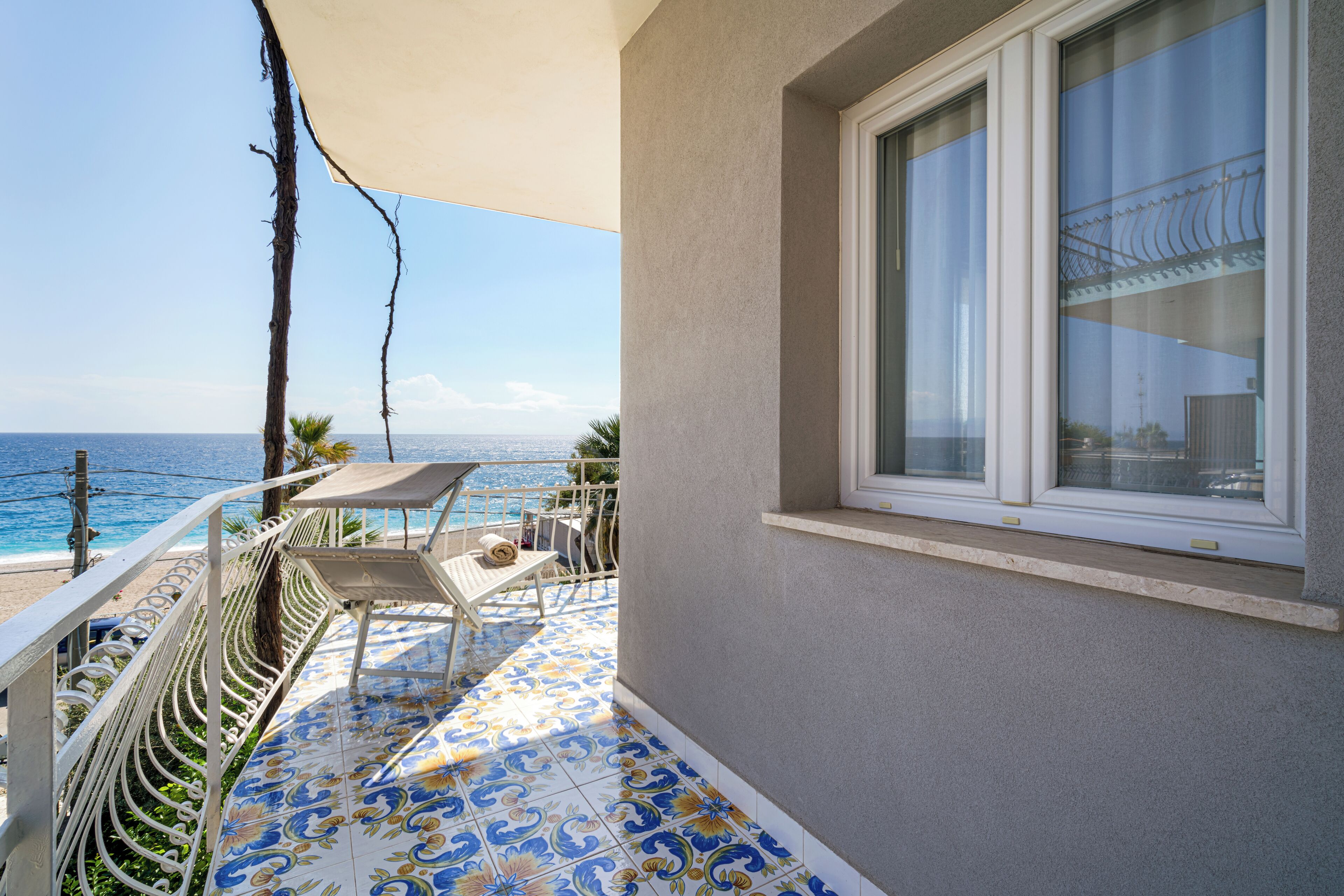 A balcony with a view of the sea, a white chair, and a table.