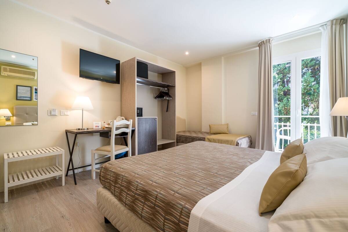 Habitación de hotel con una cama grande, un escritorio, una silla, un armario y un televisor montado en la pared.