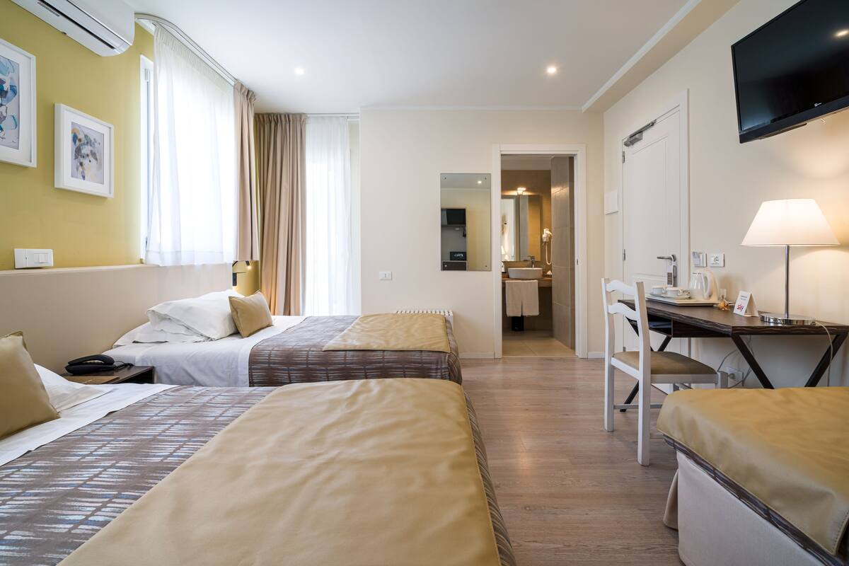 Habitación de hotel con dos camas, un escritorio, una silla, un televisor y un baño visible a través de una puerta abierta.