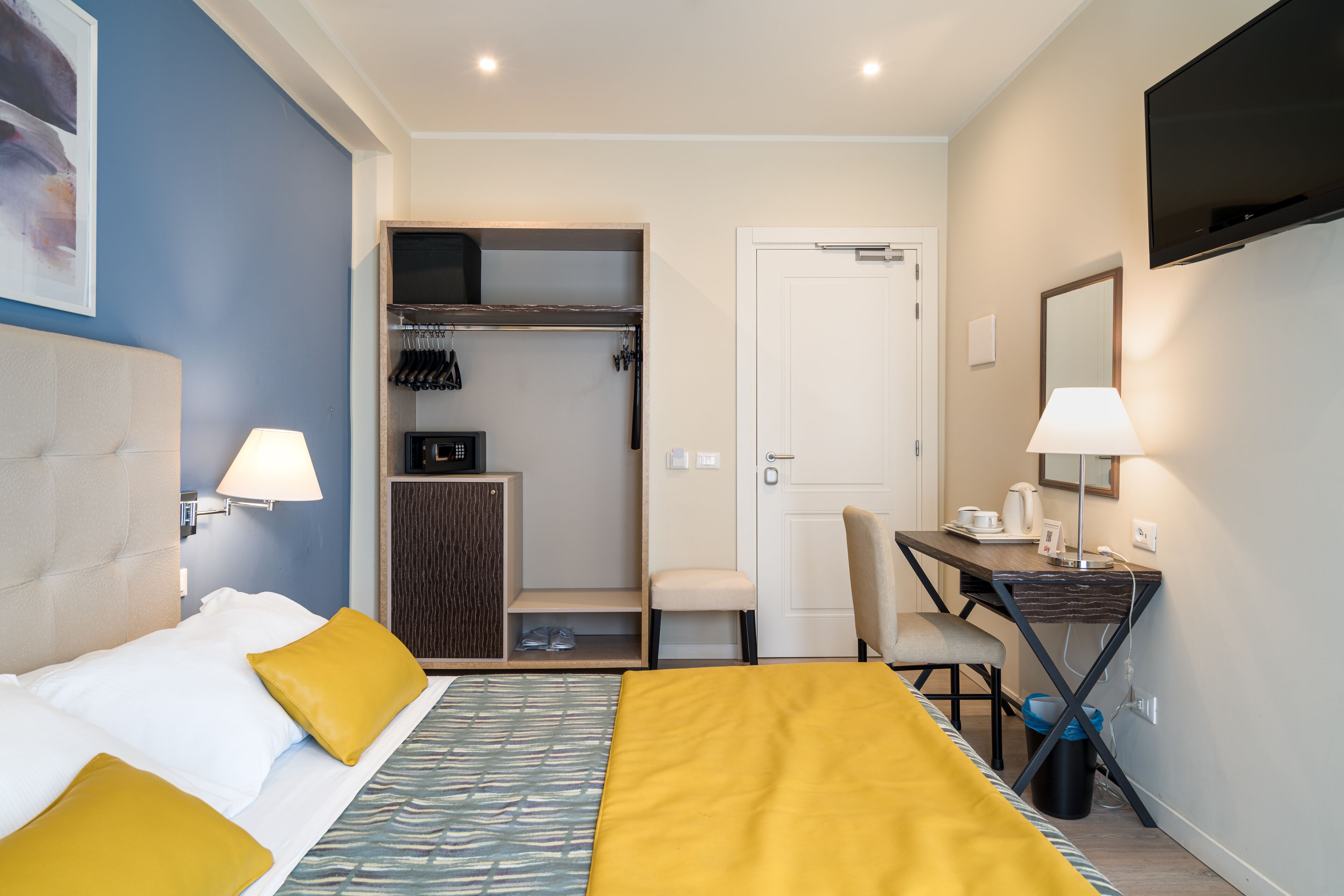 A hotel room with a bed, a desk, a chair, a wardrobe, and a television.
