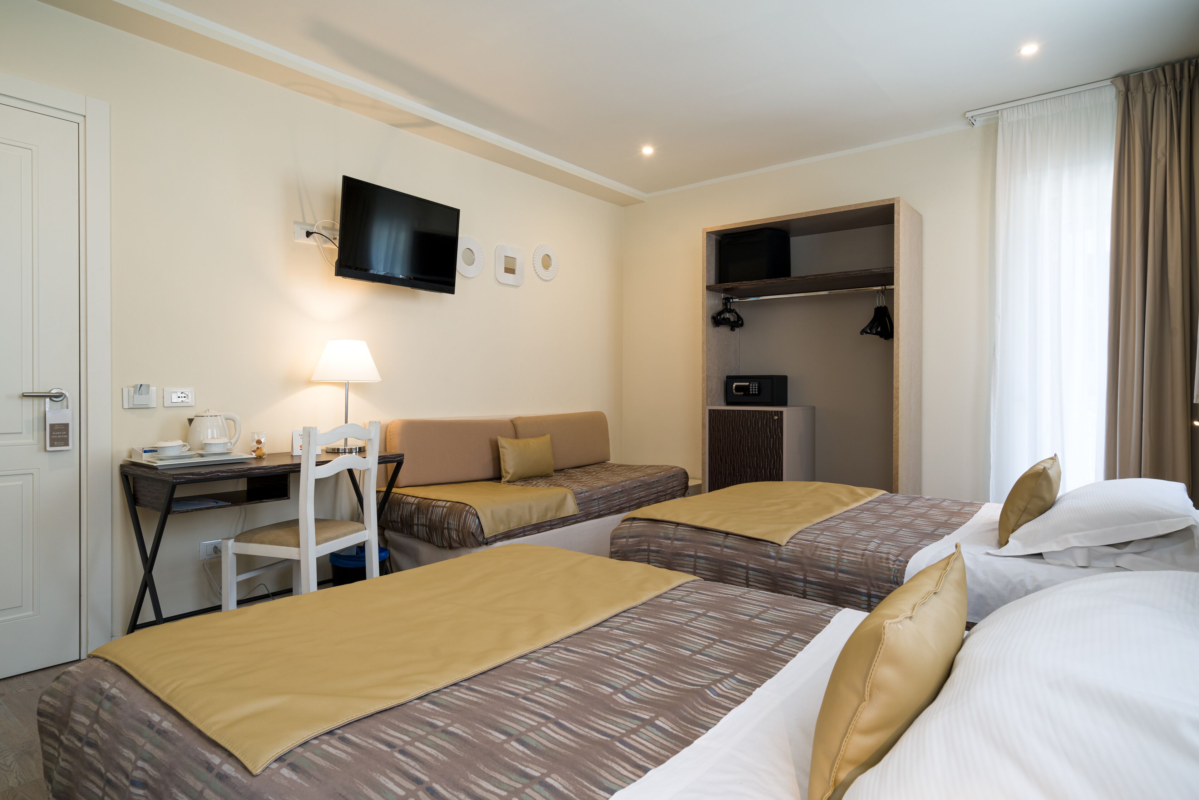 Ein Hotelzimmer mit zwei Betten, einem Schreibtisch mit Lampe, einem Fernseher und einem Kleiderschrank.