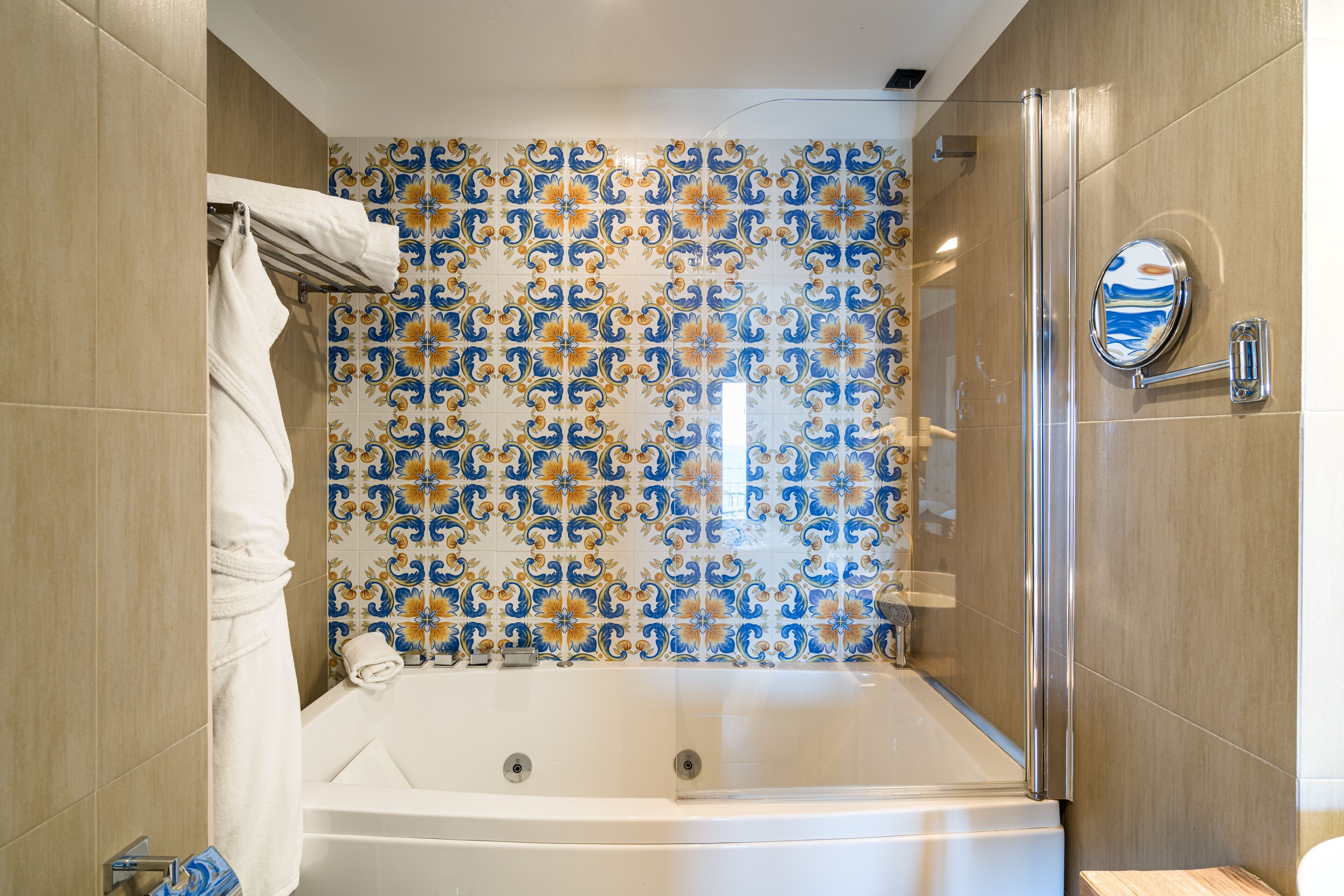 Baño con bañera, cabina de ducha de vidrio y pared de azulejos con motivos florales.