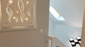 Un interior modern amb una paret de color clar, una obra d'art emmarcada, una escala i un lucernari.