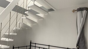 Un dormitori modern amb un llit de metall negre, roba de llit blanca i una escala de graons blancs que condueix a un espai loft.
