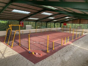 En inomhusplan för olika sporter med ett rött golv, omgiven av ett gult och svart staket, och utrustad med volleybollnät.