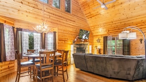 Un intérieur de chalet chaleureux avec un coin repas, un canapé, une cheminée et des murs en bois.