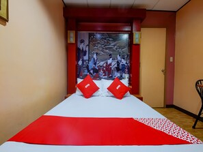 A hotel room with a bed, two red pillows, a red and white patterned bed runner, a traditional Japanese artwork on the wall, and a wooden chair. - OYO 861 Rosas Travellers Inn (Quezon City)