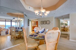 A dining area with a glass table, wicker chairs, and a chandelier. - Beachfront! Gorgeous Views! Pool, Hot Tub, Tennis Courts, Fitness Room ~ 5F Crescent Beach Club (Clearwater)