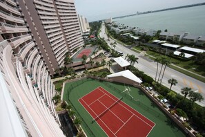 A high-rise building with multiple balconies, a tennis court, and a view of the water. - Beachfront! Gorgeous Views! Pool, Hot Tub, Tennis Courts, Fitness Room ~ 5F Crescent Beach Club (Clearwater)
