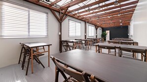 Ein Klassenzimmer mit Holztischen und -stühlen, großen Fenstern und einer Tafel.