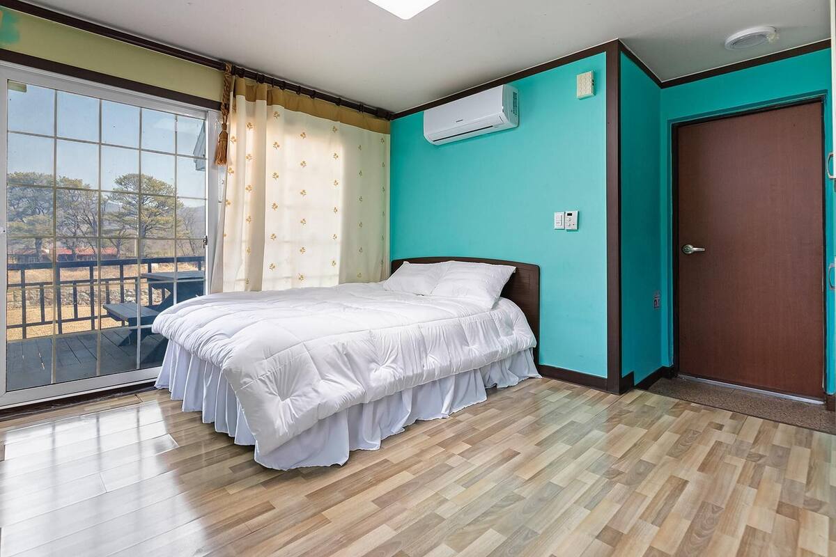 A bedroom with a bed, a sliding glass door to a balcony, and an air conditioning unit on the wall.