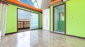 Ein geräumiges Zimmer mit Holzboden, großen Schiebeglasfenstern, die auf einen Balkon führen, und einer Duschkabine mit einer grün gefliesten Wand.