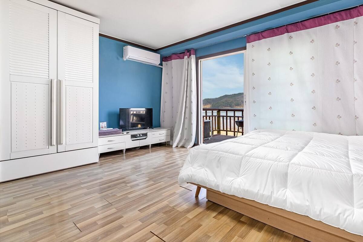 A bedroom with a bed, a TV, a wardrobe, and a balcony with a view.