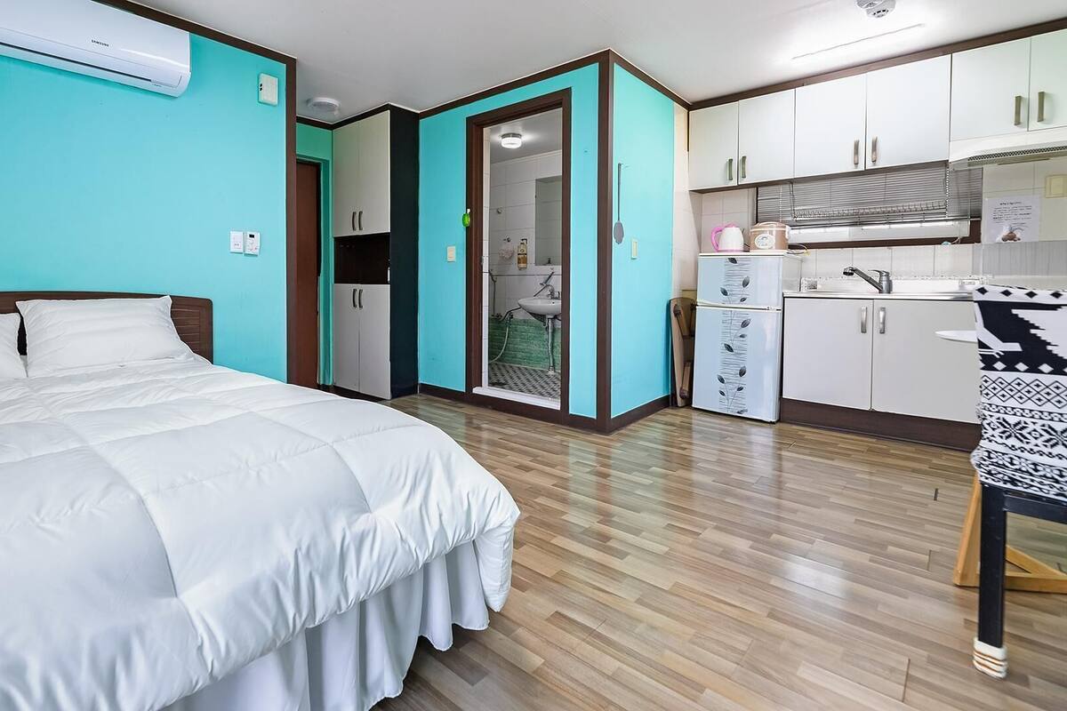 A bedroom with a bed, a kitchenette, and a bathroom.