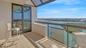 A balcony with a glass door, two white chairs, and a view of a river and cityscape.