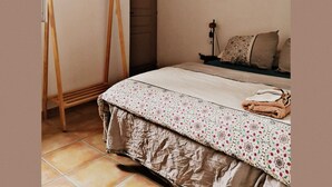 Une chambre à coucher avec un lit, un étendoir en bois, une porte et une table de chevet avec une lampe.