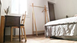 Une chambre à coucher comprenant un lit, un bureau, une chaise, un cintre en bois et une fenêtre.