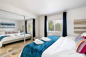 Relax in a spacious room with a large bed, full-length mirror, and a window offering a view of the outdoors.