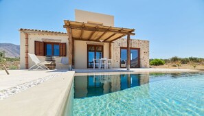 Una villa moderna con piscina, mobiliario exterior y vistas al paisaje.