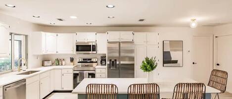 A modern kitchen with white cabinetry, stainless steel appliances, and a central island with wicker chairs.