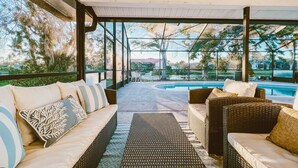 Un espacio de estar techado al aire libre con mobiliario de mimbre y vistas a una piscina.