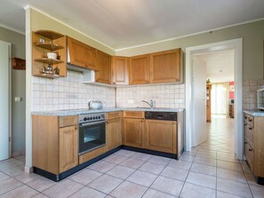 Een keuken met houten kastjes, een ingebouwde oven, een vaatwasser en een betegelde achterwand.