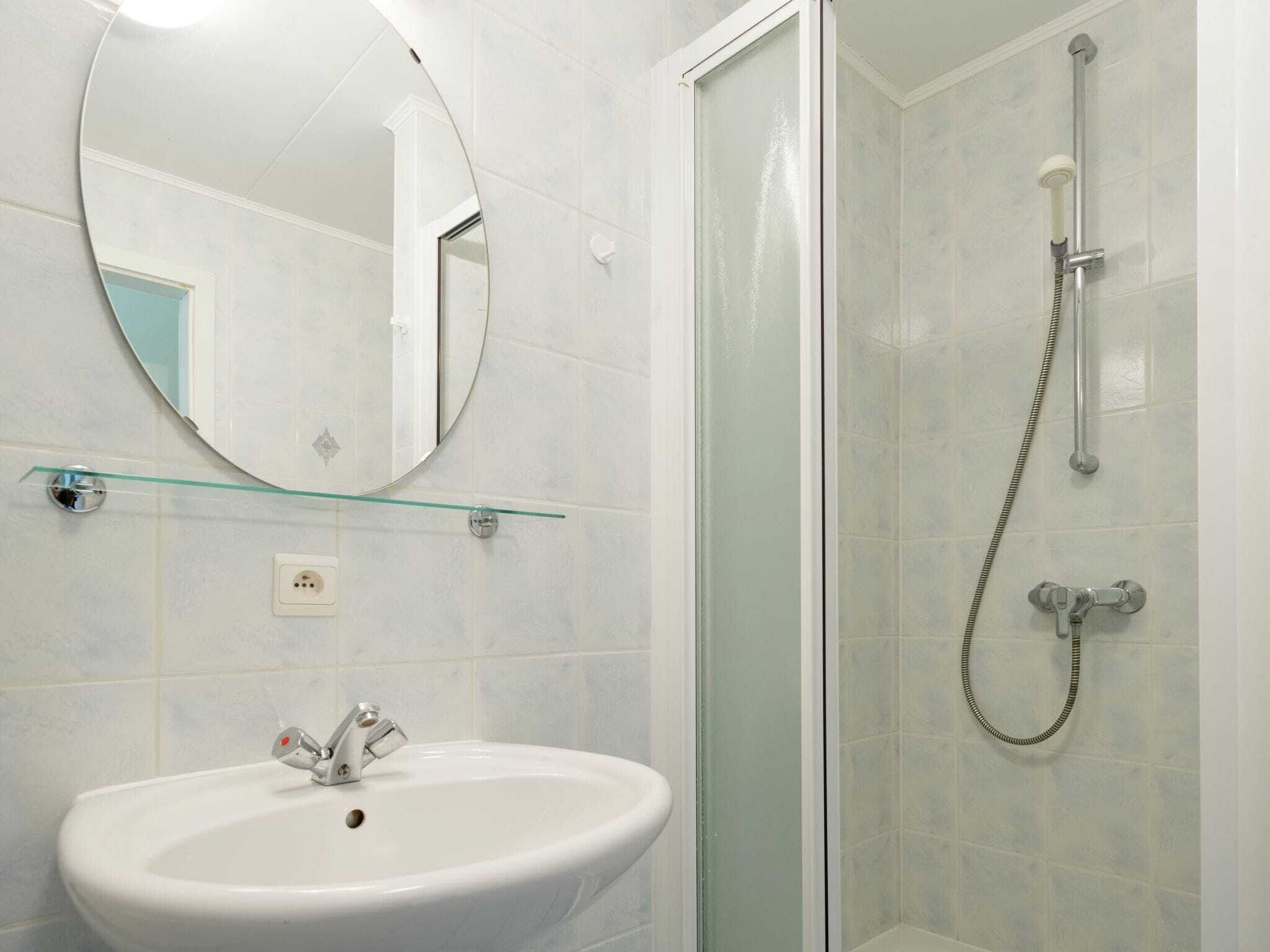 Ein Badezimmer mit einem weißen Waschbecken, einem runden Spiegel und einer Glasdusche.