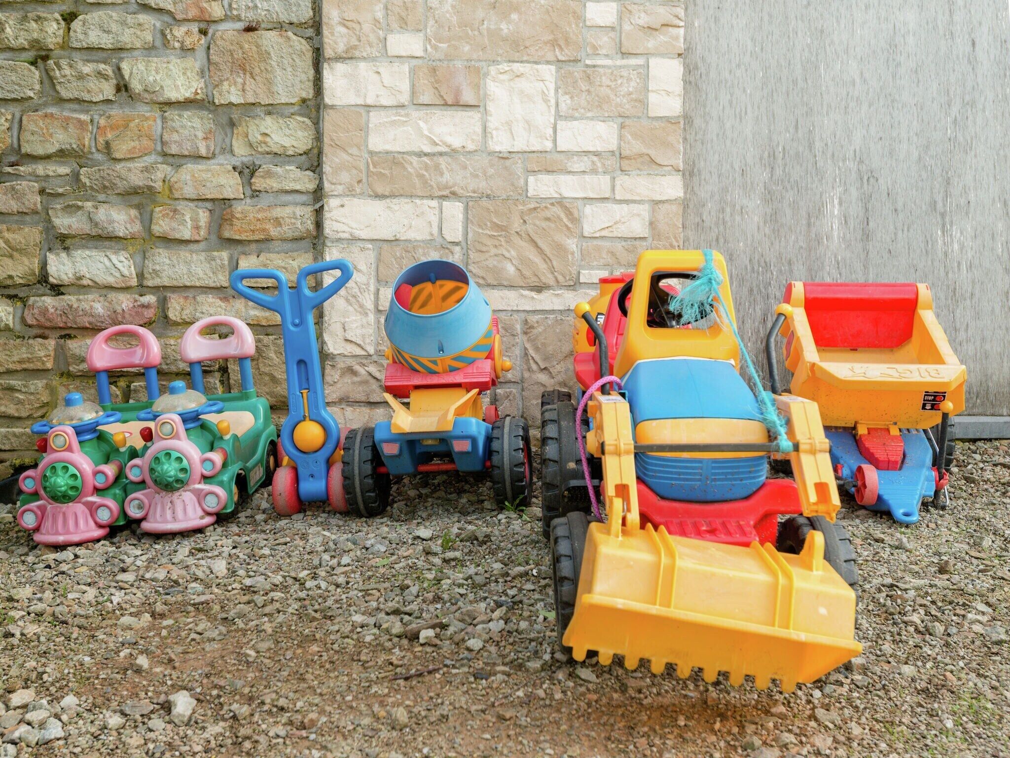 A collection of colorful toy construction vehicles parked on gravel.